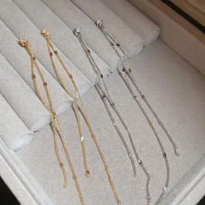 Elegant gold and silver tassel earrings with zircon studs in a grey velvet jewelry box
