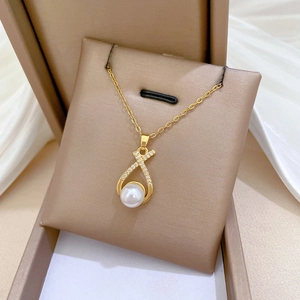 Close-up of golden pearl necklace with crisscross diamond-set pendant in a jewelry box