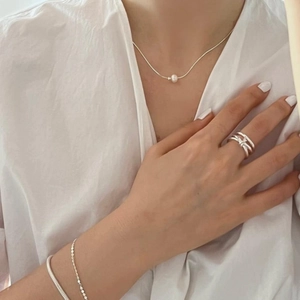 Close-up of minimalist silver knot ring with layered chain bracelets and pearl necklace