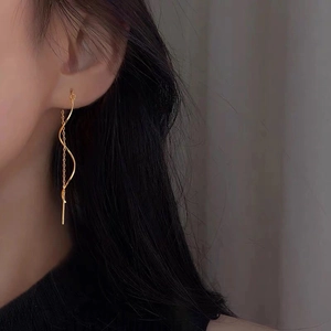 Gros plan de boucles d'oreilles pendantes vagues dorées avec perles sur l'oreille
