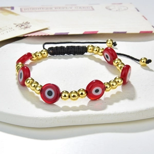 Detailed close-up of a red evil eye bead bracelet with gold accents on a black woven cord