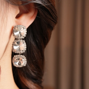 Macro detail of long silver fringe earrings with large crystals on a female model