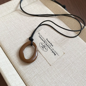Vue macro d'un pendentif géométrique en résine brune sur un cordon noir minimaliste
