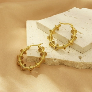 Detail of gold hollow bamboo spring hoop earrings on elegant silk and stone background