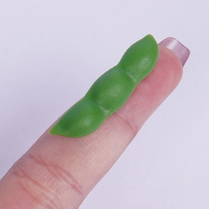 Miniature green PVC soybean pod model with realistic matte texture shown on a fingertip