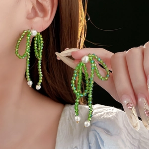 Close-up of elegant green crystal bow earrings with pearls and long tassel fringe