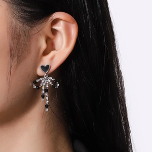 Elegant bow tassel earrings with black heart stud and sparkling crystals on model