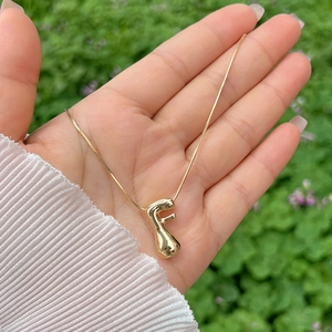 Detailed close-up of a high-polished 18K gold letter F bubble pendant on a slim chain