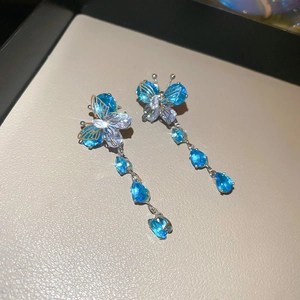 Macro shot of silver butterfly drop earrings with blue and clear zircon on leather