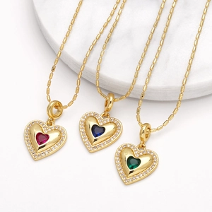 Gold heart pendant necklace with red blue green crystals on white marble base