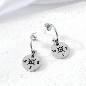 Macro detail of silver stainless steel compass earrings on white stone and satin