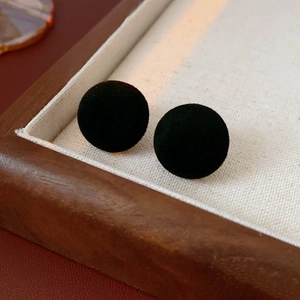 Close-up of black flocked spherical stud earrings on a cream fabric and wood tray
