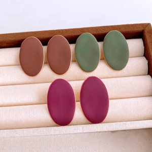 Detailed view of oval matte earrings in brown, army green, and purple on a beige jewelry tray