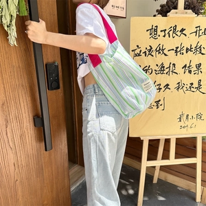 Détail d'un sac cabas en toile à rayures colorées et anses roses porté dans un café