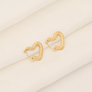 Detail of gold heart earrings with unique wavy texture on white fabric background