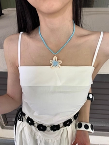 Dettaglio di collana artigianale con perline blu e ciondolo a fiore in conchiglia