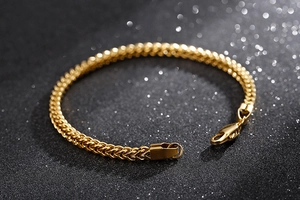 Gros plan détaillé du bracelet gourmette en acier inoxydable doré sur fond texturé