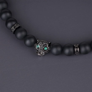 Macro detail of leopard head charm on matte black onyx bead bracelet with green eyes