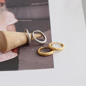 Detail view showing textured sandblasted silver and gold hoop earrings on display