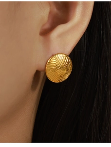 Close-up of gold-plated circular earrings with irregular wave texture worn by a model