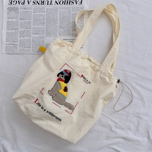Detail view of cream canvas tote bag with cartoon dog embroidery and text on soft white fabric