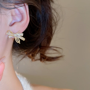 Close-up of elegant gold bow earrings with sparkling cubic zirconia on female model