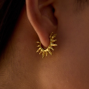 Créoles dorées en acier inoxydable avec texture de lave sur l'oreille d'un modèle