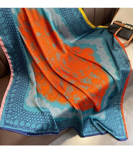 Détail d'un foulard en soie fleuri bleu et orange drapé sur un canapé en cuir marron