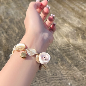 Detail of seashell charm bracelet with golden shell pendant on a beach background