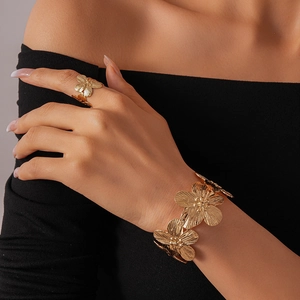 Detailed view of golden floral cuff bracelet and ring set with brushed metal texture