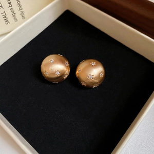 Detail of brushed 18k gold sphere earrings with zircon star inlays on jewelry box