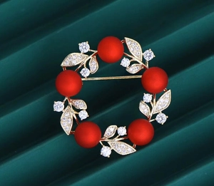 Macro shot of wreath brooch with matte red beads, golden leaves, and sparkling crystals