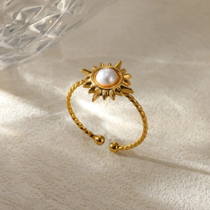 Detail of twisted gold ring band with sun design and pearl center on textured surface