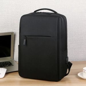 Minimalist black laptop backpack with USB charging port on a professional wooden desk setting