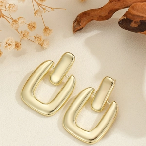 Orecchini geometrici a U in oro minimalista su sfondo vintage con texture opaca