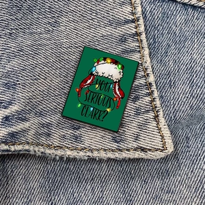 Detail of Christmas nurse enamel pin with YOU SERIOUS CLARK text on denim jacket