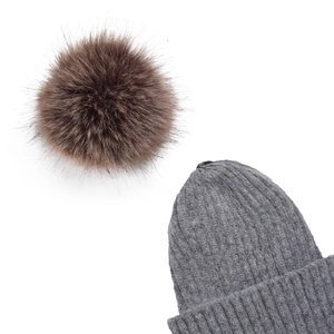 Dettaglio di un berretto in maglia a coste grigio con un soffice pompon di pelliccia marrone