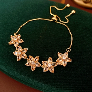 Nahaufnahme eines goldenen Blumenarmbandes mit rosa Zirkonia auf grünem Samtkasten