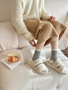 Close-up of cozy off-white plush slippers with black stripes worn in a home setting