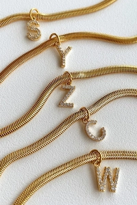 Close-up of gold snake bone chains with sparkling rhinestone initial letter pendants