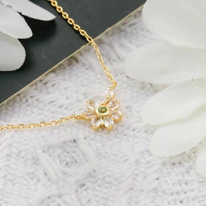 Macro shot of a floral necklace featuring gold petals with green zircon center