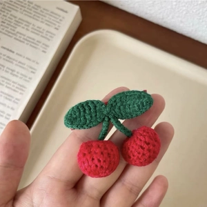 Detailed view of hand-knitted cherry hair clip with red yarn fruits and green leaves