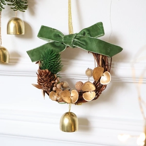 Christmas wreath with green velvet bow, pine cones, and gold bell hanging on a white wall