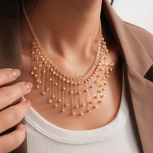 Close-up of gold fringe necklace with metallic beads layered on a brown blazer outfit