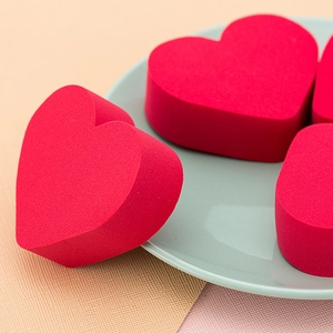 Three red heart-shaped makeup sponges on a blue ceramic plate for smooth powder application