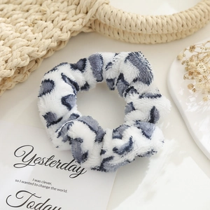 Detail of white plush scrunchie with grey leopard pattern on a minimalist desk