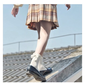 Detail of cream bow socks with lace trim worn over beige tights in outdoor lighting