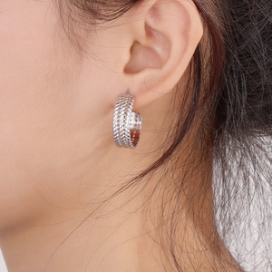 Close-up of a silver C-shaped wheat-patterned hoop earring worn on a model's ear