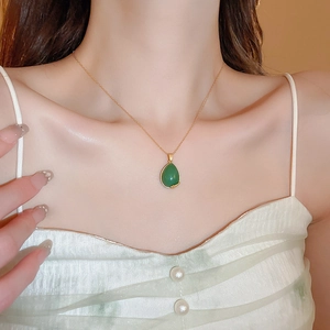 Macro detail of teardrop green stone pendant with gold-plated chain on neck