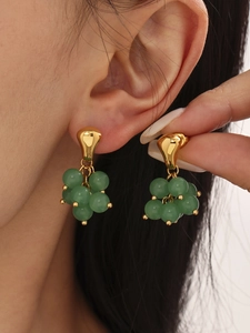 Macro shot of gold grape-shaped earrings with translucent green stone beads on the ear
